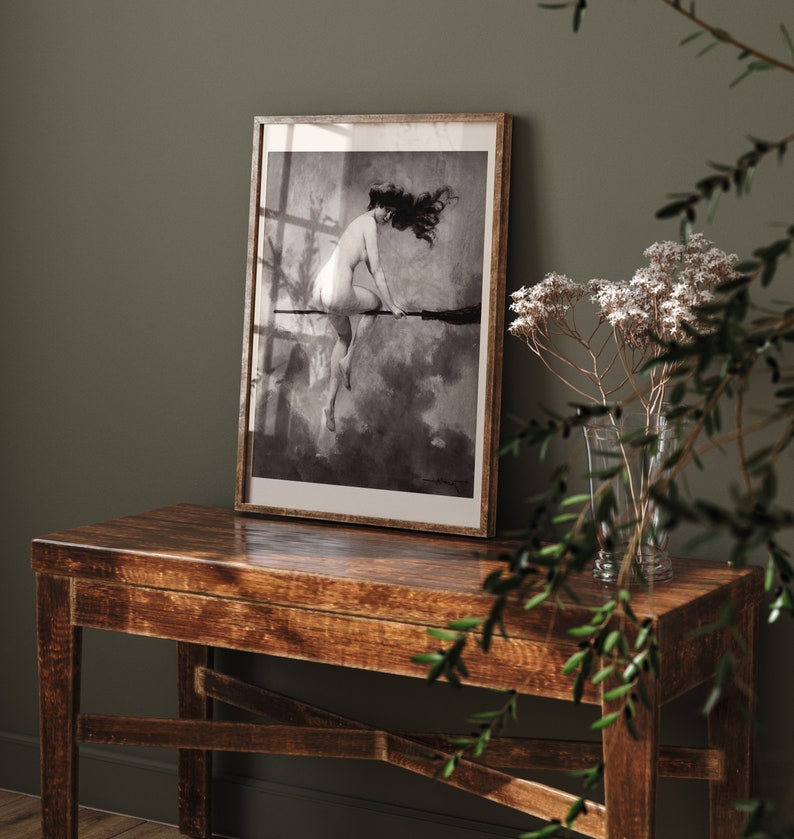 May include: A black and white framed print of a woman riding a broomstick in a cloudy sky.