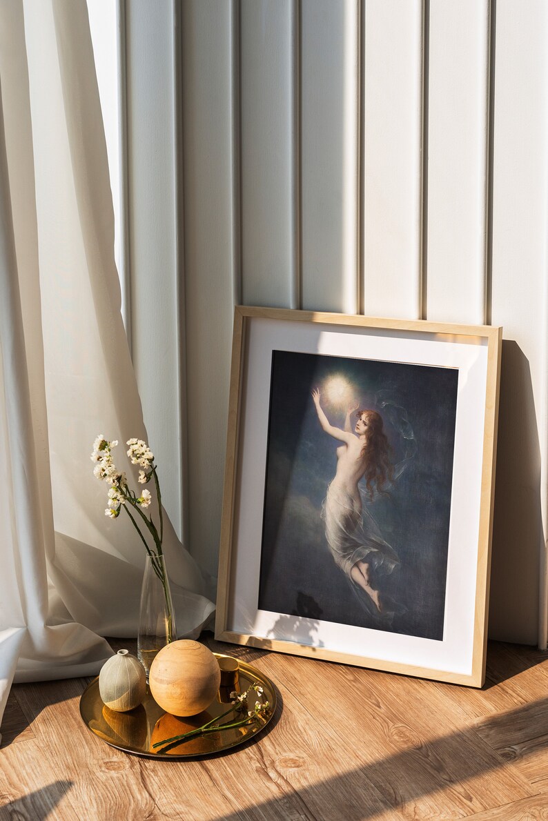May include: A framed print of a woman holding a glowing orb in a dark sky. The print is on a wooden floor with a gold tray, a small white vase with white flowers, and a wooden sphere.