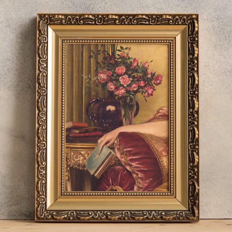 May include: A framed painting of a woman in a pink and gold dress sitting in a chair. She is holding a book in her hand. There is a vase of pink roses on a table behind her.