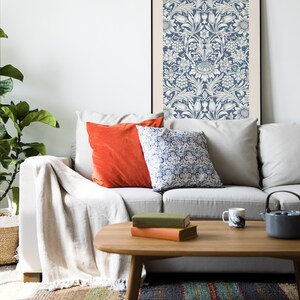 May include: A white couch with a throw blanket and two patterned pillows. A framed print with a blue and white floral pattern hangs on the wall above the couch. A wooden coffee table with books and a mug sits in front of the couch.
