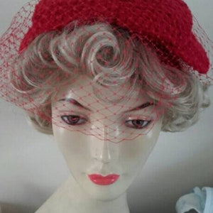 May include: A red crocheted hat with a matching veil. The hat is worn on a mannequin with blonde hair.