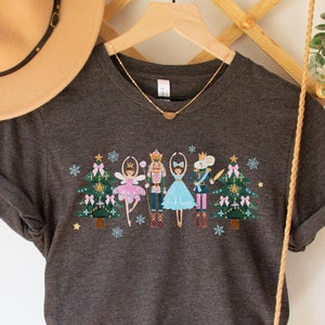 May include: Dark grey heather t-shirt with a colorful embroidered design of a Nutcracker and Sugar Plum Fairy dancing in front of a Christmas tree.