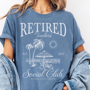 Puede incluir: Camiseta azul con el texto "RETIRED Teachers Social Club" y un gr&aacute;fico de playa. El gr&aacute;fico incluye palmeras, un sol, una sombrilla y el a&ntilde;o "2025". La camiseta es de estilo casual.