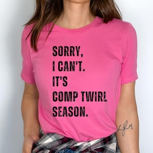 May include: Pink t-shirt with the text "SORRY, I CAN'T. IT'S COMP TWIRL SEASON."