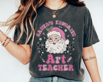 May include: A dark gray t-shirt with a pink and white graphic design featuring Santa Claus with the text "Santa's Favorite Art Teacher".