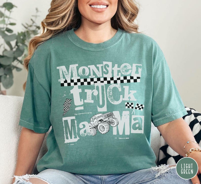 May include: A light green t-shirt with the words "Monster Truck Mama" in a distressed white font. The design includes a monster truck graphic and checkered flag accents. The shirt is a relaxed fit.
