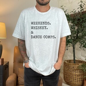 May include: A gray t-shirt with the text "Weekends. Whiskey. & Dance Comps." printed on the front.