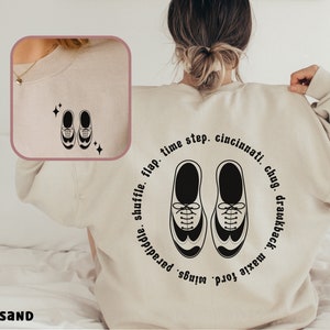 May include: A beige sweatshirt with a black graphic of two shoes and text that reads "time step. cincinnati chug. drawkback. maxie ford. wings. paradiddle. shuffle. flap."