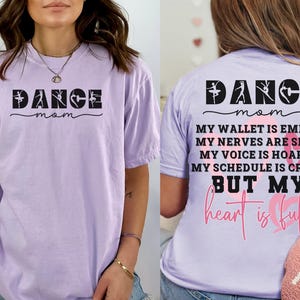 May include: A light purple short-sleeve t-shirt. The front features the black text DANCE mom with ballet silhouettes. The back displays DANCE mom, MY WALLET IS EMPTY, MY NERVES ARE SHOT, MY VOICE IS HOARSE, MY SCHEDULE IS CRAZY BUT MY heart is full.