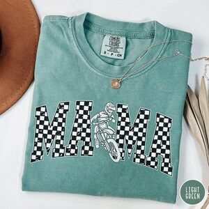 Peut inclure: T-shirt vert clair avec un graphique "MAMA" &agrave; carreaux repr&eacute;sentant un pilote de motocross. Le t-shirt est fait d'un tissu doux et confortable.