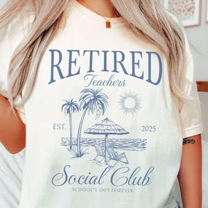 Puede incluir: Camiseta color marfil con un gr&aacute;fico azul. El gr&aacute;fico dice "Retired Teachers Social Club" con elementos de escena de playa: palmeras, sol, tumbonas y el a&ntilde;o 2025. La camiseta es de estilo casual.