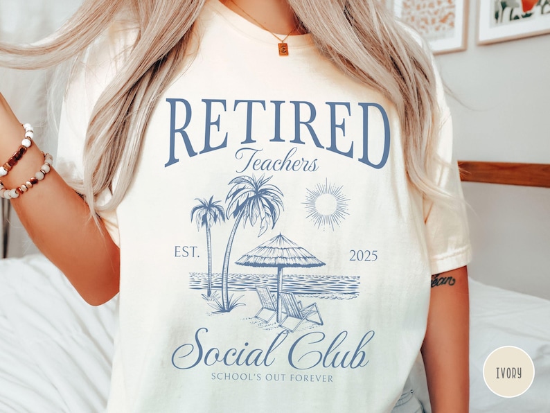 Puede incluir: Camiseta color marfil con un gr&aacute;fico azul. El gr&aacute;fico dice "Retired Teachers Social Club" con elementos de escena de playa: palmeras, sol, tumbonas y el a&ntilde;o 2025. La camiseta es de estilo casual.