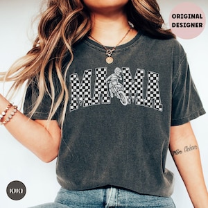 Peut inclure: Un t-shirt noir avec un motif &agrave; carreaux qui &eacute;pelle "MAMA" avec un pilote de motocross au milieu du mot. Le t-shirt a un aspect vieilli.