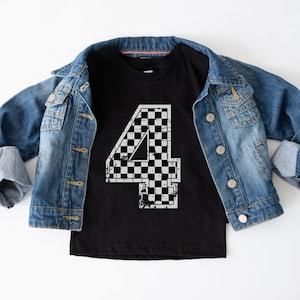 Pu&ograve; includere: T-shirt nero girocollo con un grande numero 4 a scacchi bianchi e neri usurato. La maglietta &egrave; esposta su una giacca di jeans blu chiaro.