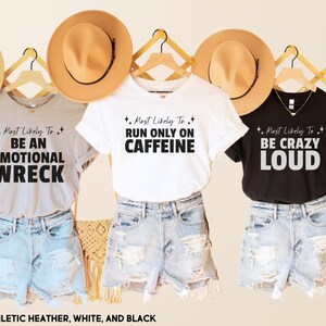 May include: Three t-shirts with different sayings on them. The first shirt is gray and says "Most Likely To Be An Emotional Wreck". The second shirt is white and says "Most Likely To Run Only On Caffeine". The third shirt is black and says "Most Likely To Be Crazy Loud".