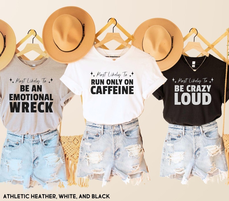 May include: Three t-shirts with different sayings on them. The first shirt is gray and says "Most Likely To Be An Emotional Wreck". The second shirt is white and says "Most Likely To Run Only On Caffeine". The third shirt is black and says "Most Likely To Be Crazy Loud".