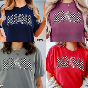 Peut inclure: Un t-shirt avec un motif &agrave; carreaux et le mot "MAMA" en lettres blanches. Le motif comprend &eacute;galement une silhouette d'un pilote de motocross. Le t-shirt est disponible en quatre couleurs : marine, baie, gris et rouge.