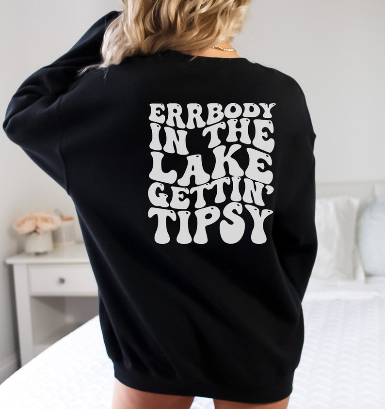 May include: Black sweatshirt with white text on the back that reads "ERRBODY IN THE LAKE GETTIN' TIPSY" in a retro font. The sweatshirt is a solid black color and has long sleeves.