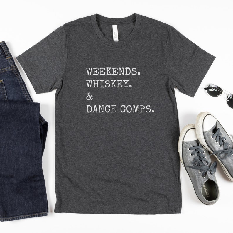 May include: A dark heather grey t-shirt with the text "WEEKENDS. WHISKEY. & DANCE COMPS." printed in white.