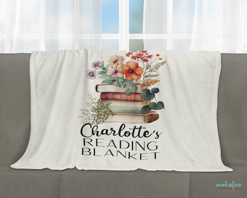 May include: A white fleece blanket with a floral design and a stack of books. The text "Charlotte's Reading Blanket" is printed on the blanket.