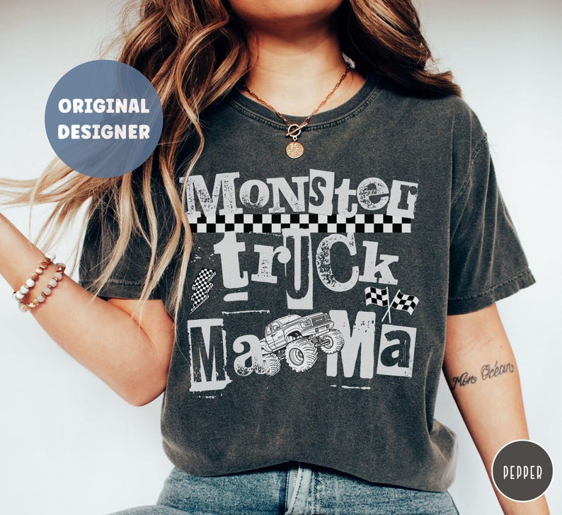 May include: Dark gray t-shirt with the words "Monster Truck Mama" in a distressed, vintage style. The design includes a monster truck graphic and checkered flag details. The shirt has a round neck and short sleeves.