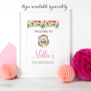 Puede incluir: Un letrero de cumplea&ntilde;os enmarcado con una ilustraci&oacute;n de erizo en acuarela. El letrero dice "Welcome to Millie's 8th Birthday" con detalles florales. Dos decoraciones de papel de nido de abeja y un sobre rosa est&aacute;n en primer plano.
