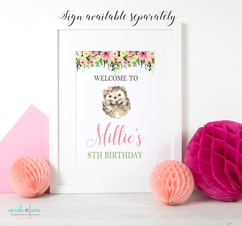 Puede incluir: Un letrero de cumplea&ntilde;os enmarcado con una ilustraci&oacute;n de erizo en acuarela. El letrero dice "Welcome to Millie's 8th Birthday" con detalles florales. Dos decoraciones de papel de nido de abeja y un sobre rosa est&aacute;n en primer plano.