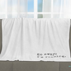 May include: White fleece throw blanket with black text that reads "go away, I'm reading."