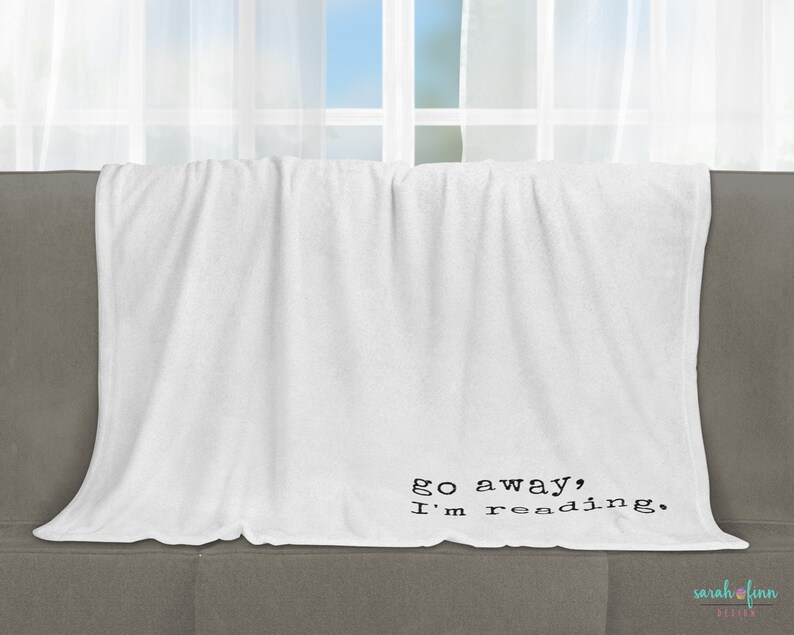 May include: White fleece throw blanket with black text that reads "go away, I'm reading."