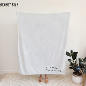 May include: A white fleece throw blanket with the text "go away, I'm reading." printed in black.