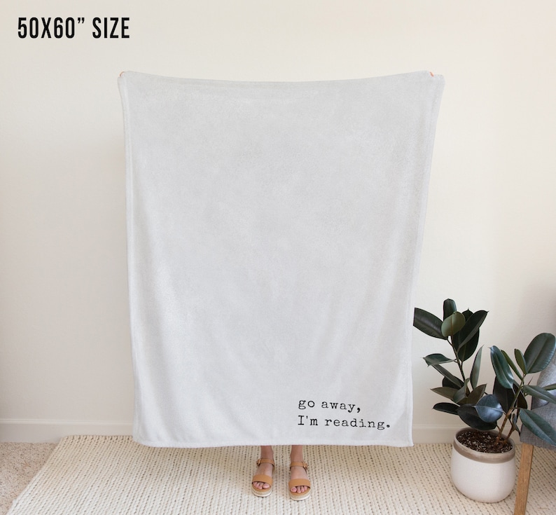 May include: A white fleece throw blanket with the text "go away, I'm reading." printed in black.