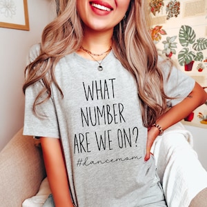May include: Gray t-shirt with the text "WHAT NUMBER ARE WE ON?" and the hashtag "#dancemom" printed in black.