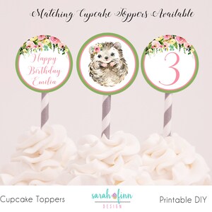 Puede incluir: Tres adornos para cupcakes con dise&ntilde;os florales y de erizos. Uno dice "Happy Birthday Emilia", otro presenta un erizo con una corona floral, y el tercero tiene el n&uacute;mero "3". Cada uno est&aacute; sobre una pajita a rayas.