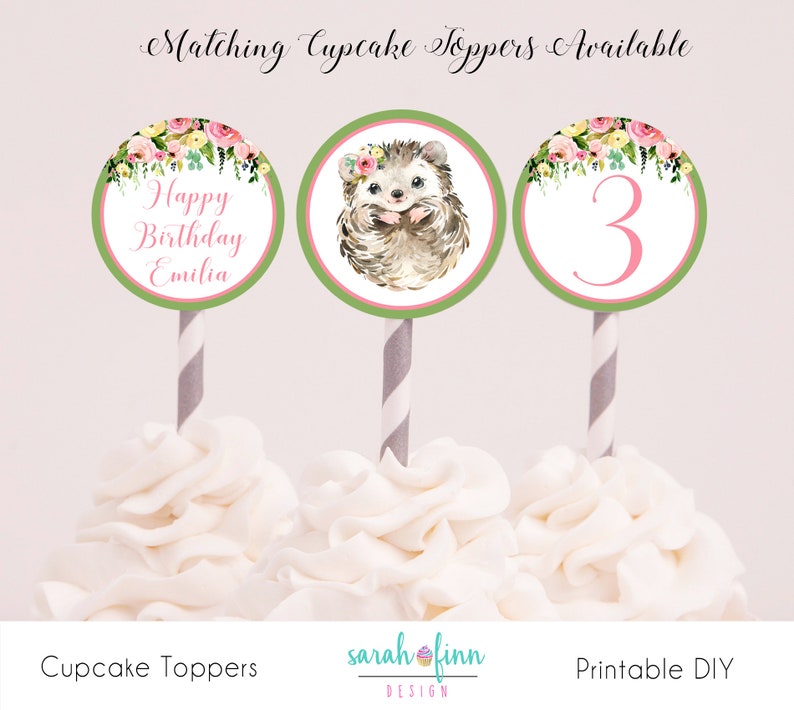 Puede incluir: Tres adornos para cupcakes con dise&ntilde;os florales y de erizos. Uno dice "Happy Birthday Emilia", otro presenta un erizo con una corona floral, y el tercero tiene el n&uacute;mero "3". Cada uno est&aacute; sobre una pajita a rayas.