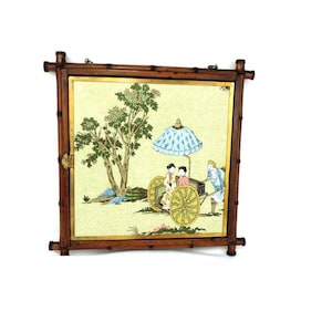 以下が含まれることがあります： 青と白の傘の下、カートに乗った人々の絵が描かれた、竹製の額縁付きの壁掛け。緑の木々と薄い黄色の空を背景に、風景が描かれている。