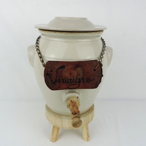 May include: White ceramic vinegar crock with a wooden lid, wooden base with three legs, and a wooden sign that reads "Vinaigre".