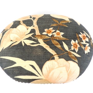 Puede incluir: Un puf redondo con estampado floral negro y blanco con un diseño de flores crema.