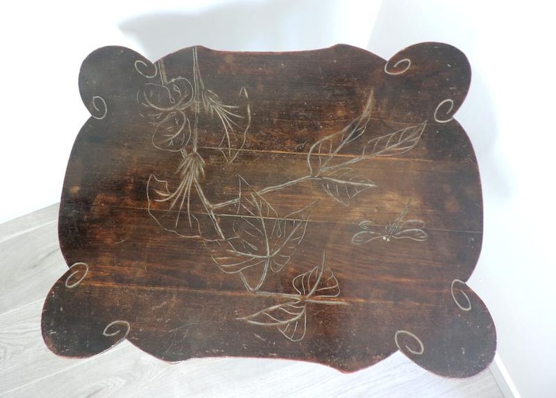 Puede incluir: Una mesa de madera de color marr&oacute;n oscuro con borde festoneado y superficie rectangular. La superficie presenta un dise&ntilde;o grabado de hojas, flores y una lib&eacute;lula, con patrones de espirales decorativos tallados en cada una de las cuatro esquinas.