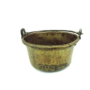 May include: A small, antique brass pot with a single iron handle. The pot has a worn, aged patina and is marked with a number.