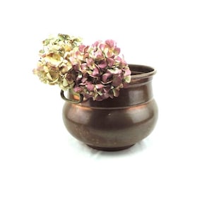 May include: A copper planter with a rounded shape and a handle. The planter is filled with dried hydrangeas in shades of pink and white.
