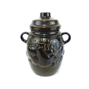 May include: A brown ceramic jar with a lid, featuring a raised design of fruit and the word "Frucht" on the front.