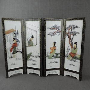 Peut inclure: Écran pliable à quatre panneaux avec des scènes peintes de personnages et de paysages asiatiques. Les panneaux sont blancs avec des bordures noires et des accents décoratifs. Chaque panneau représente une scène différente.