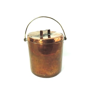 以下が含まれることがあります： 蓋と真鍮製の取っ手のある銅のバケツ。バケツはくすんでいて、使い古したような外観です。