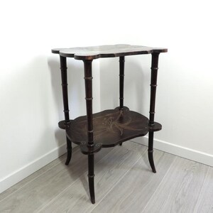 Puede incluir: Una mesa auxiliar de dos niveles en color marr&oacute;n oscuro con un dise&ntilde;o de bordes festoneados. Las cuatro patas presentan una textura segmentada estilo bamb&uacute;. Ambas superficies est&aacute;n decoradas con un delicado patr&oacute;n floral incrustado.