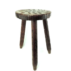 May include: A rustic wooden stool with three legs and a round top. The stool is made of dark brown wood and has a natural, unfinished look.