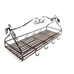 May include: A distressed metal wall shelf with a rectangular basket and six hooks. The shelf has a decorative, curved top with leaf accents and a distressed white and brown finish. Ideal for kitchen or bathroom storage.