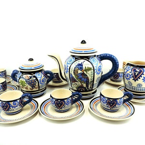 Puede incluir: Un juego de té de cerámica azul y blanco con una tetera, una jarra de crema, un azucarero y seis tazas y platillos. El juego presenta un diseño de pájaro colorido y detalles florales.