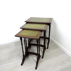 Puede incluir: Un conjunto de tres mesas nido con marcos de madera oscura y tapas de cuero verde.