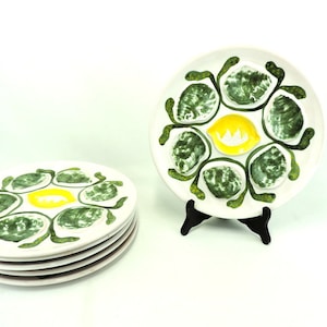 May include: Set of four white ceramic oyster plates with green and yellow painted details. Each plate features six individual oyster shells and a lemon slice in the center.