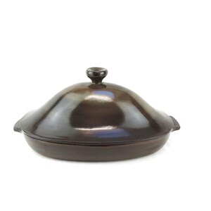 Könnte beinhalten: Eine braune Keramik-Backform mit Deckel. Die Form ist oval und hat eine glatte, glänzende Oberfläche. Der Deckel hat einen kleinen Knopf oben.